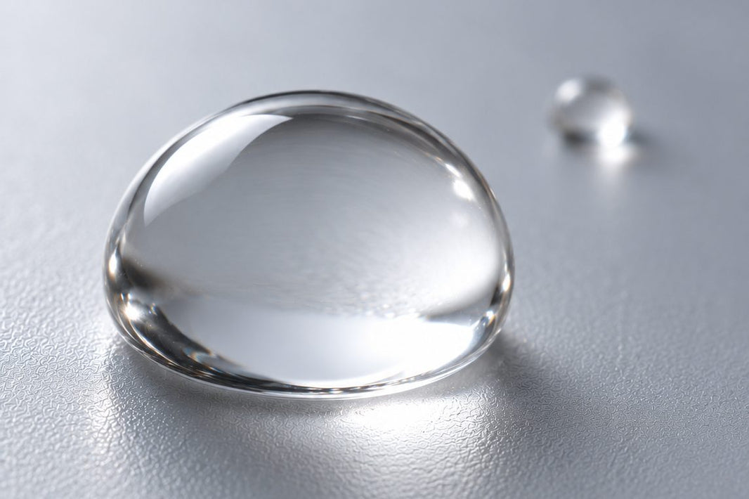 Una grande goccia d'acqua trasparente e una molto più piccola su superficie grigia, a richiamare l'alto e il basso peso molecolare dell'acido ialuronico