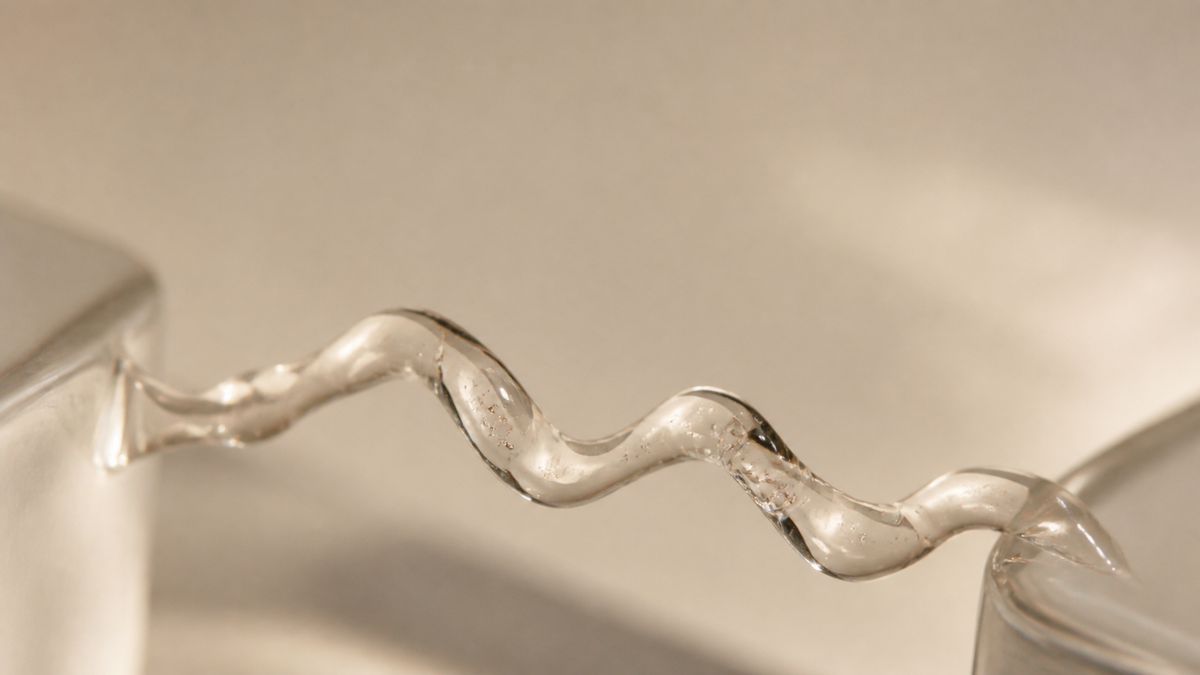 Filamento di gel traslucido sospeso tra due superfici di vetro, immagine dell'articolo sulla differenza tra polinucleotidi e PDRN